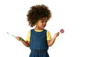 childhood and people concept- lovely african american little girl with toothbrush and sweet lolipop. Healthy teeth concept. Unhealthy food. photo