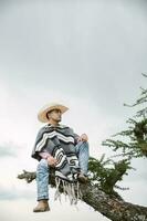 Cowboy wearing a poncho sitting under a tree in the sky photo