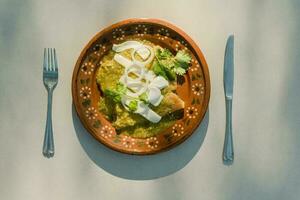 saborear el auténtico mexicano sabor de verde enchiladas servido en un plato con cubiertos foto
