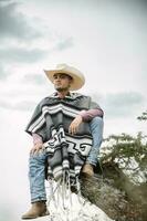 Cowboy wearing a poncho sitting under a tree in the sky photo