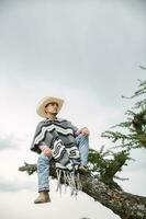 Cowboy wearing a poncho sitting under a tree in the sky photo