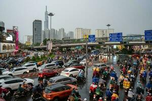 Ho Chi Minh, Viet Nam - 24 April 2023 Vietnamese people wear helmet and raincoat ride motorbike in heavy rain and traffic jam. photo