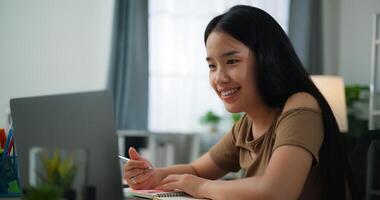 oung Asian woman working with a laptop and writing on paper on a desk photo