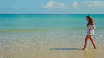 une fille dans blanc des promenades le long de le plage avec bleu l'eau. video