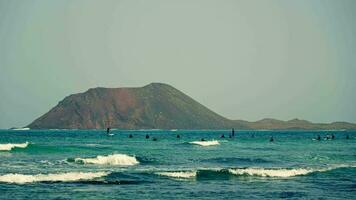 People surfers, riding against the backdrop of a volcanic island video