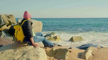 un' ragazza con un' giallo zaino su il mare si siede. video