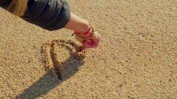 A girl's hand draws a heart in the sand video