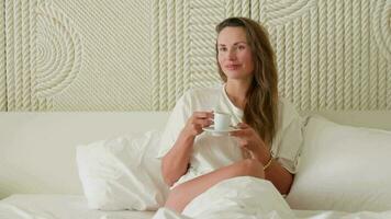 A girl drinks coffee in bed in the morning, a white room. video