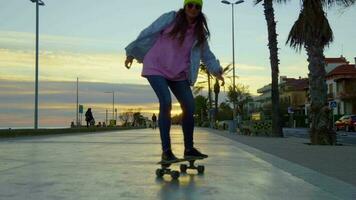 A girl rides a skateboard against the backdrop of a sunset video