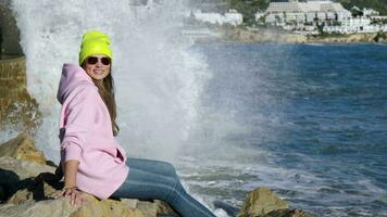 The girl sits against the background of breaking waves on the rocks video