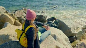 Girl with a yellow backpack sitting on rocks by the sea video