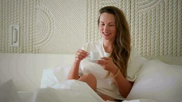 menina com uma copo do café dentro cama, feliz manhã. video