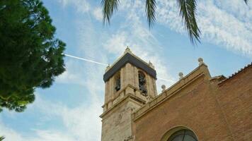 A tower against the sky, birds flying around, a palm leaf in the foreground. video