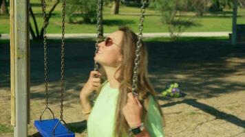 A girl in sunglasses swings on a swing. video