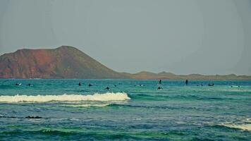 Surfers are waiting for waves far out to sea, against the backdrop of the island video