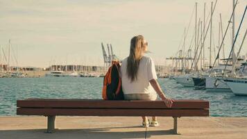 il ragazza si siede su un' panchina nel il mare marina con yacht. video