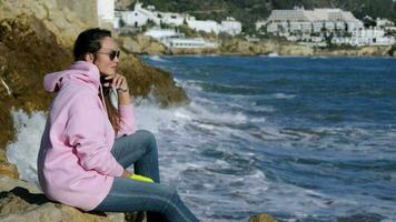 The girl sits against the background of breaking waves on the rocks video