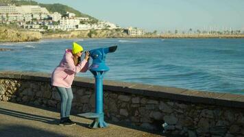 un niña mira dentro un telescopio en el costa de el mar video