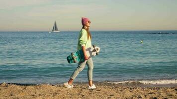 un joven niña camina con un patinar a lo largo el mar. video