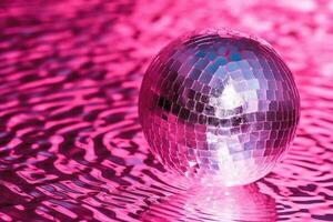 Disco ball on pink. Silver disco ball in water with light reflections. photo