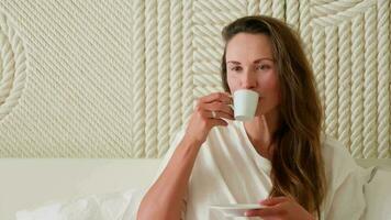 Girl with dark hair drinking coffee in bed. video