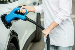 Young business woman refueling her electric car at a EV charging station. Concept of environmentally friendly vehicle. Electric car concept. Green travelling. photo