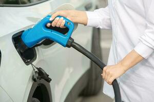 Young business woman refueling her electric car at a EV charging station. Concept of environmentally friendly vehicle. Electric car concept. Green travelling. photo