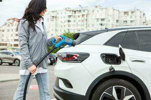 Young business woman refueling her electric car at a EV charging station. Concept of environmentally friendly vehicle. Electric car concept. Green travelling. photo