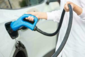 Young business woman refueling her electric car at a EV charging station. Concept of environmentally friendly vehicle. Electric car concept. Green travelling. photo