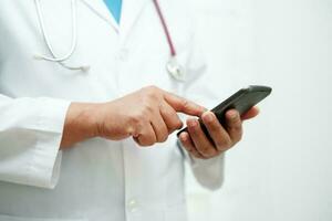 asiático mujer médico participación móvil teléfono o tableta para buscar método de tratamiento paciente en hospital. foto