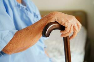 Asian elderly disability woman patient holding walking stick in wrinkled hand at hospital. photo