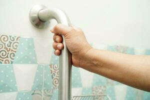 Asian woman patient use toilet support rail in bathroom, handrail safety grab bar, security in nursing hospital. photo