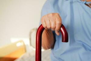 Asian elderly disability woman patient holding walking stick in wrinkled hand at hospital. photo