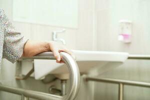 Asian elderly old woman patient use toilet support rail in bathroom, handrail safety grab bar, security in nursing hospital. photo