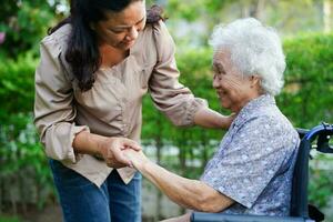 Caregiver help Asian elderly woman disability patient sitting on wheelchair in park, medical concept. photo