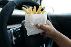 Asian woman driver hold and eat french fries in car, dangerous and risk an accident. photo