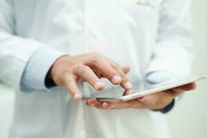 asiático hombre médico utilizando tableta computadora a leyendo paciente informe, cheque arriba y buscar para resolver tratamiento salud médico en línea en hospital. foto