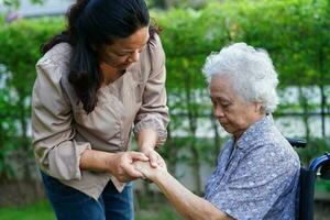 cuidador ayuda a una anciana asiática con discapacidad a una paciente sentada en silla de ruedas en el parque, concepto médico. foto