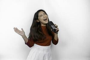 Portrait of carefree Asian woman, having fun karaoke, singing in microphone while standing over white background photo