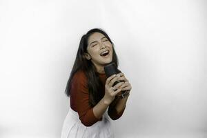 Portrait of carefree Asian woman, having fun karaoke, singing in microphone while standing over white background photo