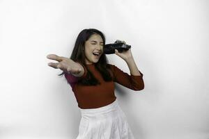 Portrait of carefree Asian woman, having fun karaoke, singing in microphone while standing over white background photo