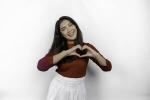 A happy young Asian woman wearing a red t-shirt feels romantic shapes heart gesture expresses tender feelings photo