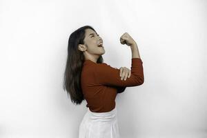 emocionado asiático mujer vistiendo un rojo parte superior demostración fuerte gesto por levantamiento su brazos y músculos sonriente con orgullo foto