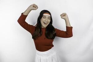 A young Asian woman with a happy successful expression wearing red top and flag headband isolated by white background. Indonesia's independence day concept. photo