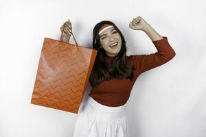 Happy young Asian woman is smiling while bringing shopping bag, isolated on white background. Indonesian independence day sale concept photo