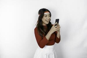 A portrait of a smiling Asian woman wearing headband and holding her phone, isolated by white background. Indonesia's independence day concept photo