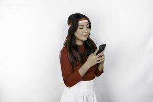 A portrait of a smiling Asian woman wearing headband and holding her phone, isolated by white background. Indonesia's independence day concept photo