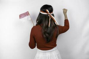 espalda ver de un joven asiático mujer con un contento exitoso gesto vistiendo rojo parte superior y bandera venda aislado por blanco antecedentes. de indonesia independencia día concepto. foto