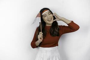 Happy smiling Indonesian woman holding Indonesia's flag and showing love sign to celebrate Indonesia Independence Day isolated over white background. photo