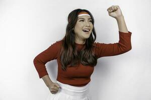 A young Asian woman with a happy successful expression wearing red top and flag headband isolated by white background. Indonesia's independence day concept. photo